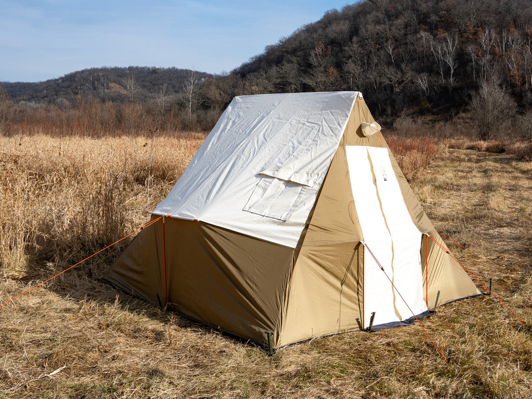 Beige tent  in a field with trees in the background