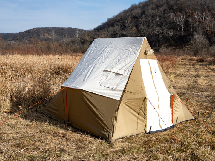 Beige tent  in a field with trees in the background