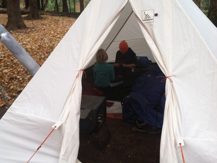 Snowtrekker 10x13 Crew setup in fall with leaves on the ground door open wood stove to the left with two children playing in the tent on ground pads