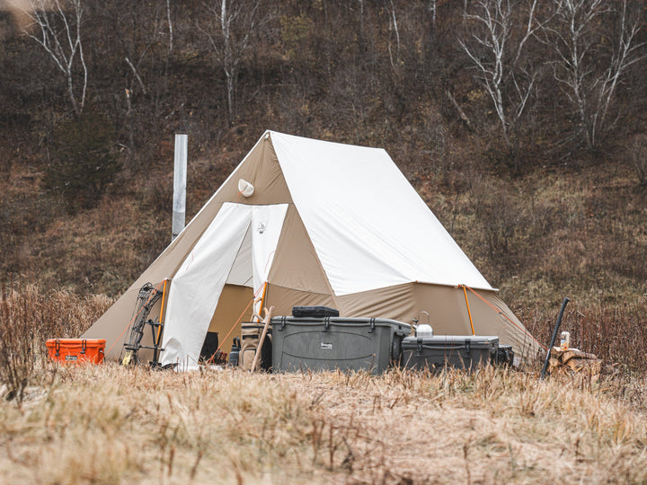 Beige bell tent in a natural setting with trees and dry grass.