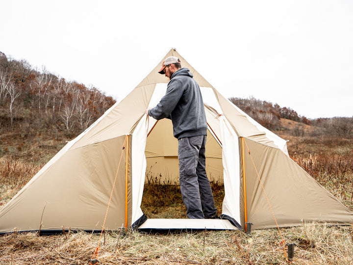Person setting up a beige tent in a natural outdoor setting