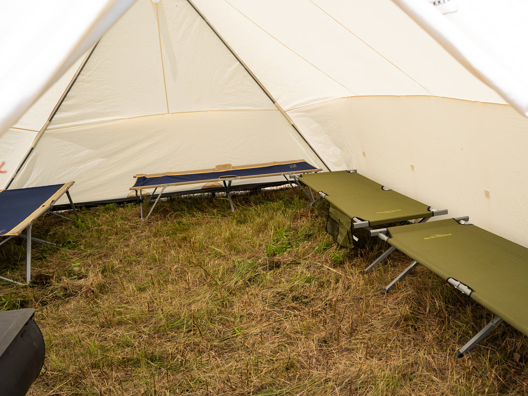 Tent with multiple green camping cots on a grassy ground