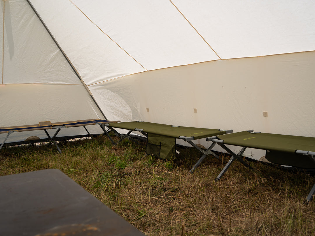 Camping scene with green cots against a white canvas tent in an outdoor setting