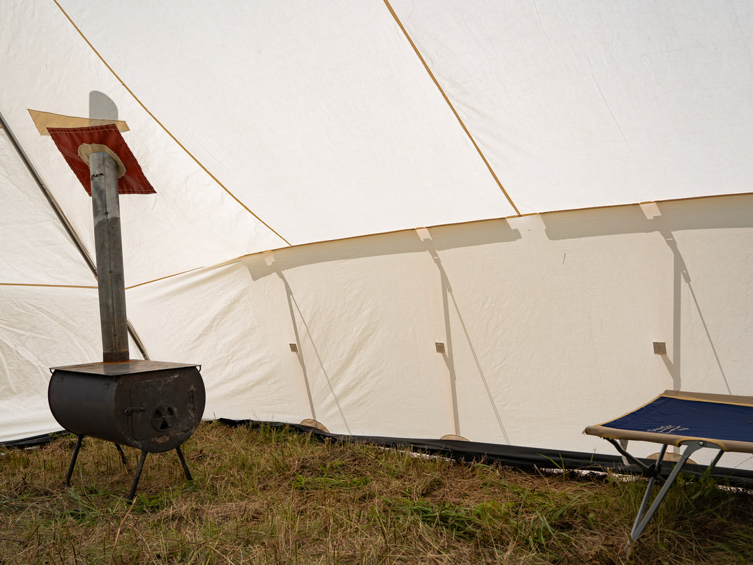 White canvas tent with a wood stove and chair in an outdoor setting