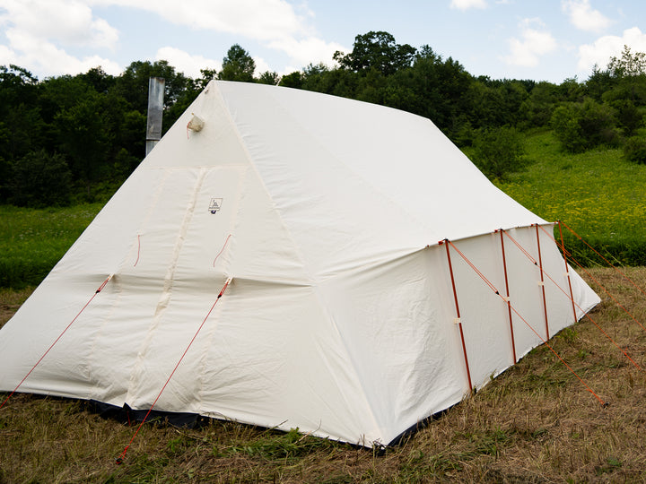 White canvas tent with orange guy out ropes on a grassy field with trees in the background