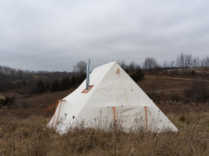 White canvas tent in a field with a cloudy sky