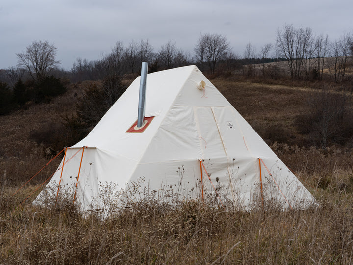 White canvas tent with a chimney in a field on a cloudy day
