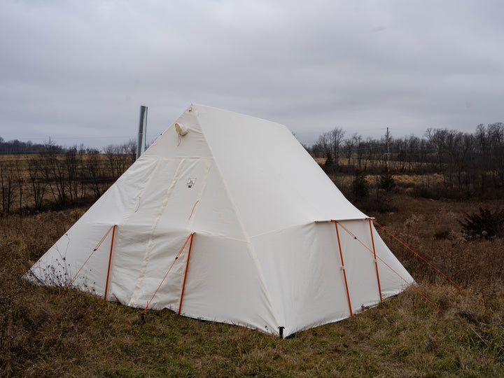 White canvas tent with orange guy out ropes and poles in a field on a cloudy day
