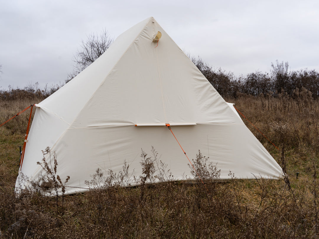 White canvas tent set up in a field with a cloudy sky