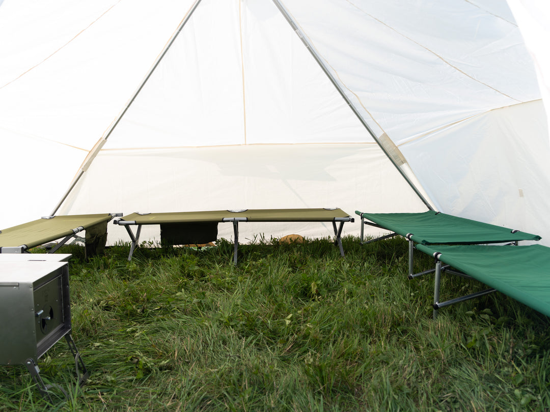 Green camping cots in front of a large white tent on grass