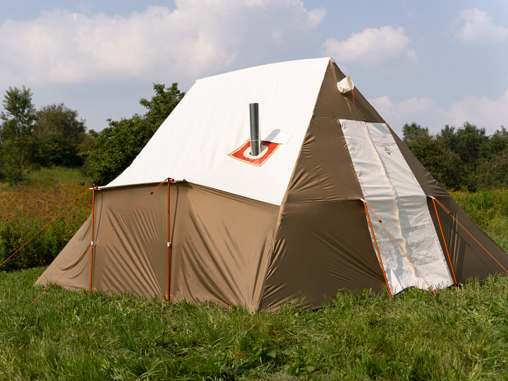 Brown nylon and white canvas tent with a chimney on a grassy field