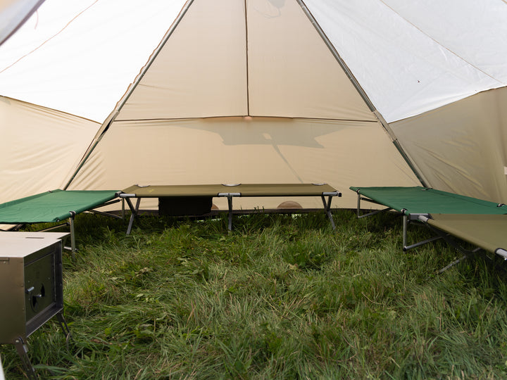 Brown tent with green camping cots on grass
