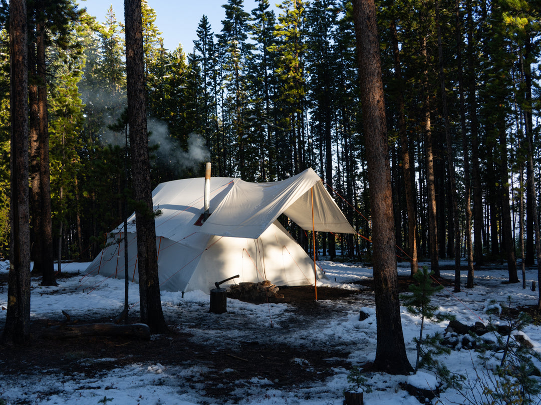 White canvas tent in a snowy forest with smoke rising from chimney
