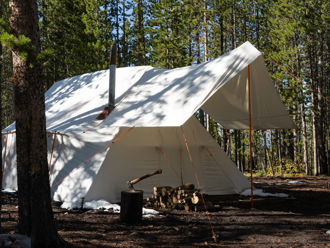 White canvas tent  with vestibule in a forest setting with trees and ground visible