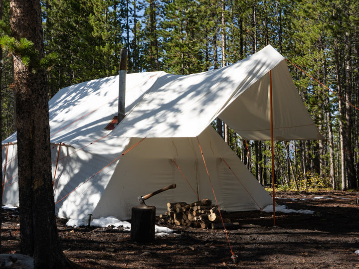White canvas tent  with vestibule in a forest setting with trees and ground visible