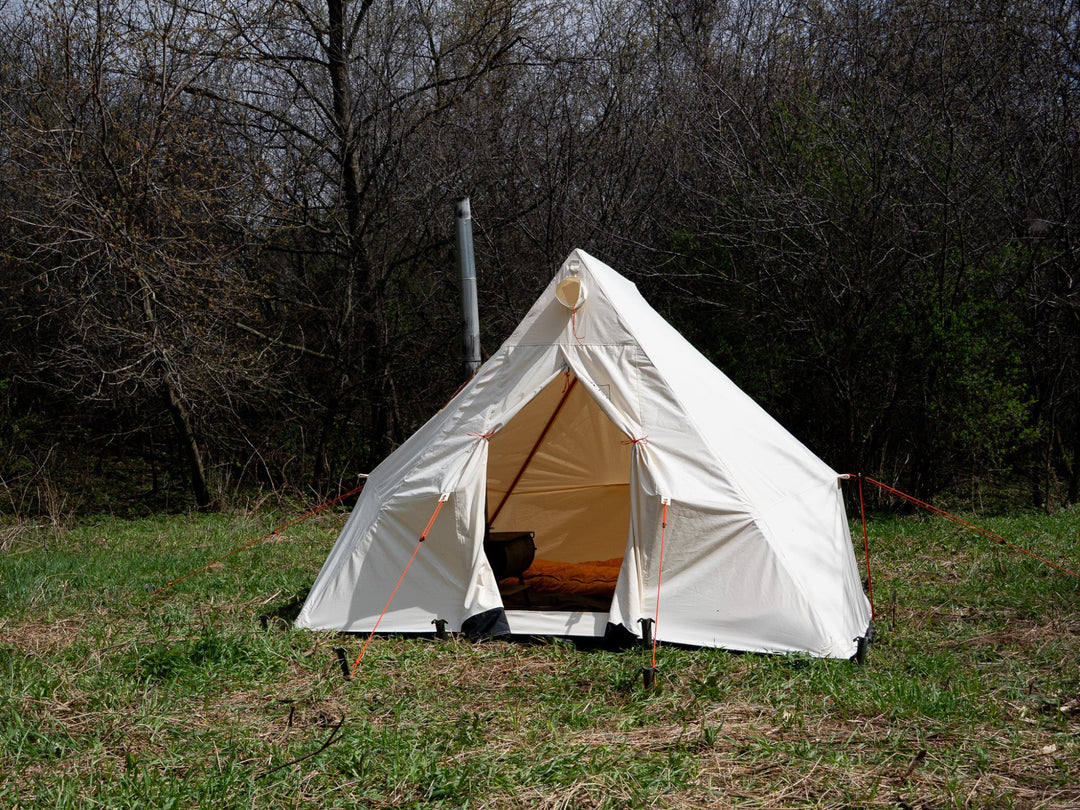White camping tent in a grassy area with trees in the background