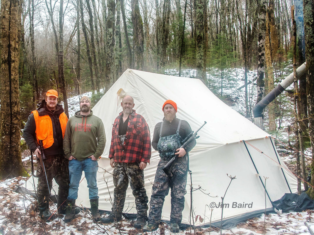 Snowtrekker 13x15 Mega Crew Setup In Woods With Four Men Standing In Front Of Tent two holding hunting rifles