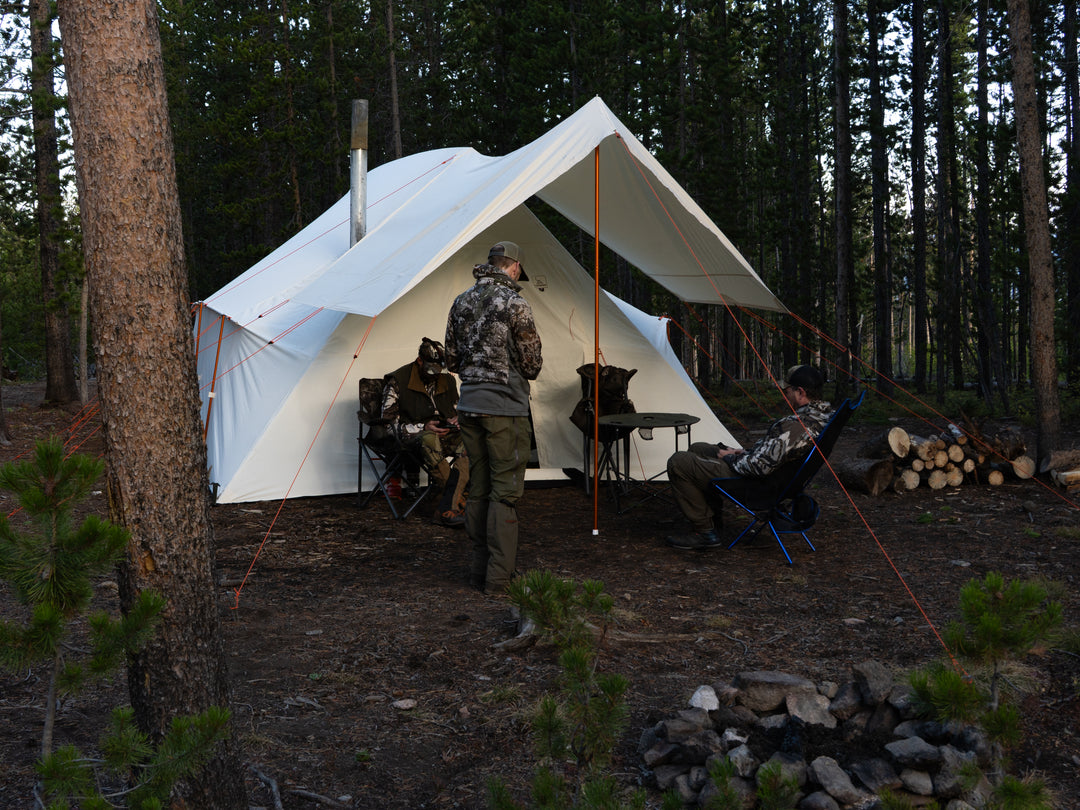Three people camping in a forest with a large white canvas hot tent.