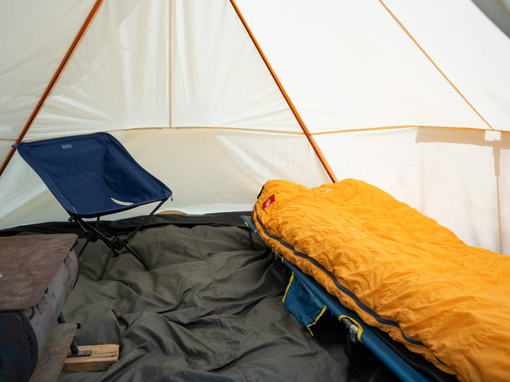 Camping setup inside a tent with a blue chair, gray sleeping pad, and yellow sleeping bag.