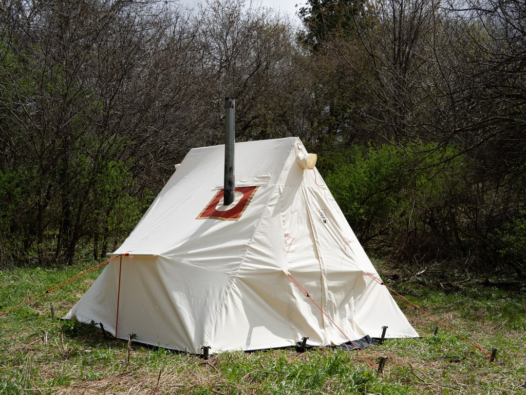 White canvas tent with a chimney in a forest setting