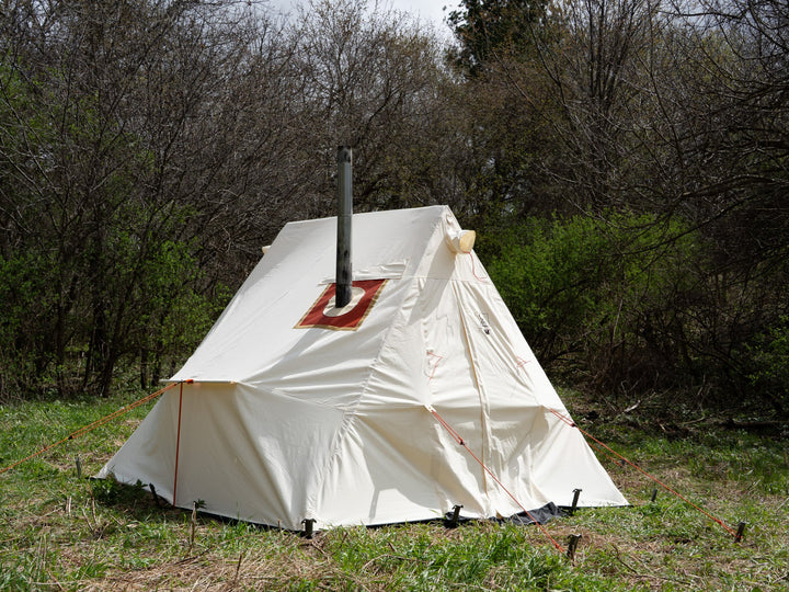 White canvas tent with a chimney in a forest setting