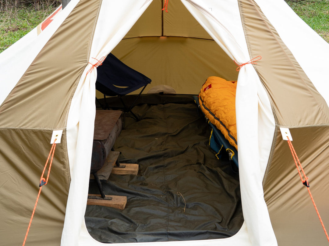 Open beige tent with camping gear inside, including a sleeping bag and chair.