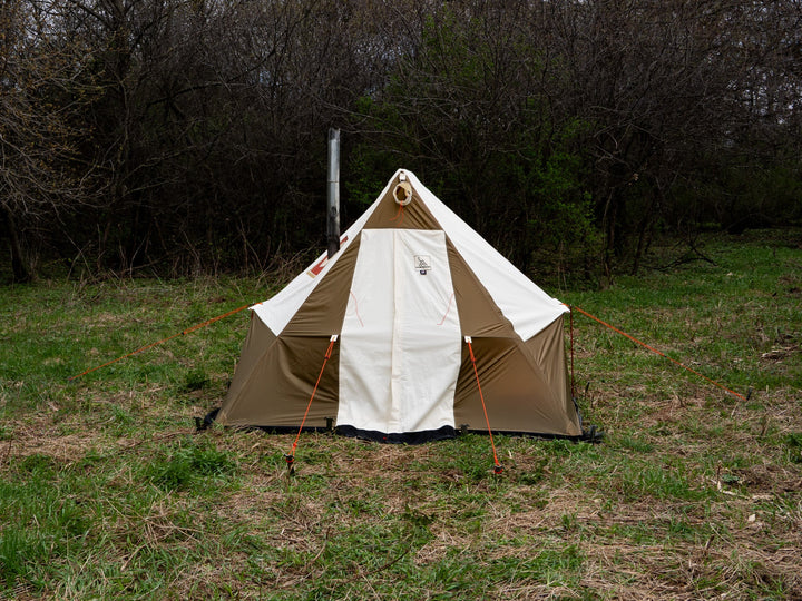 Brown and white tent in a grassy field with trees in the background