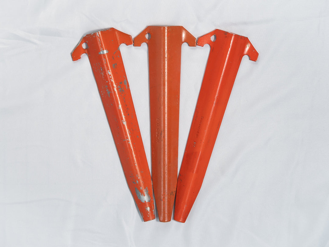 Three orange aluminum tent stakes on a white background