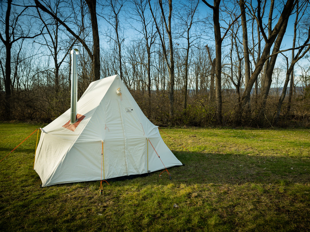 Snowtrekker 9.5x9.5 High Country front view chimney exiting left side of tent spark arrester on top setup on green grass with trees in background