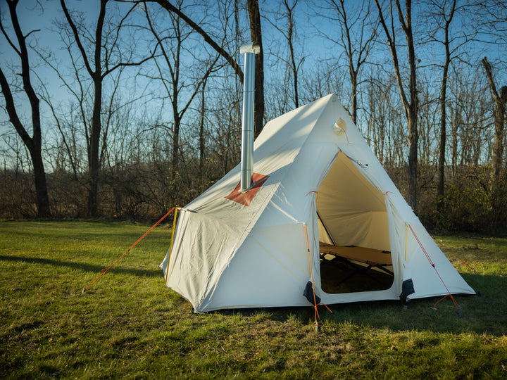 Snowtrekker High Country Base Model stove pipe exiting tent vertically on left side door open tan cot along right sidewall trees in background