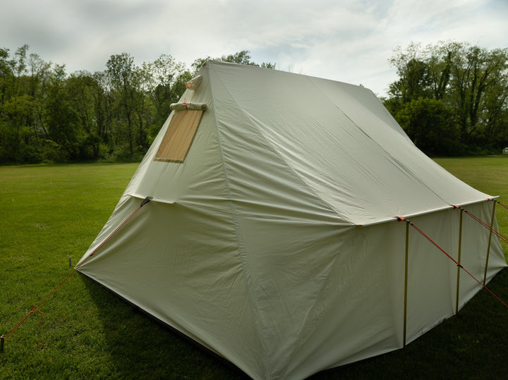 SNowtrekker 10x13 Outfitter setup on green grass with trees in background looking at the back of the tent with Screen Window In Tent canvas window cover rolled up and tied in place with orange rope