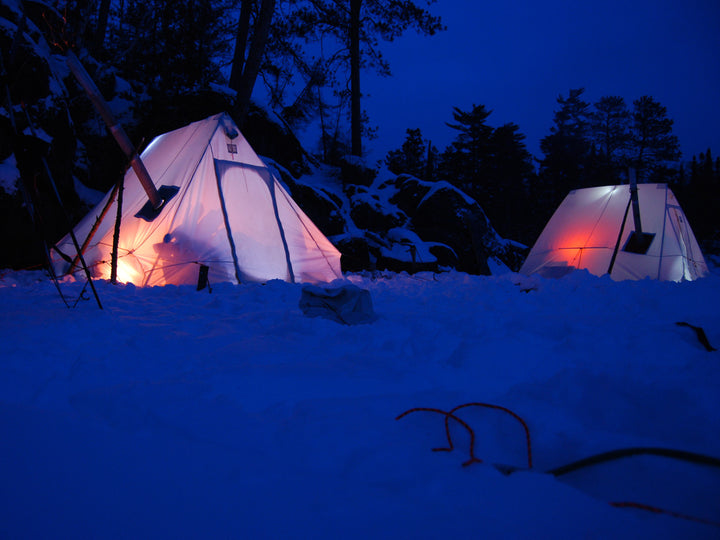 Snowtrekker 9x11.5 Crew In Winter Lights in Tent snow on ground with rock face and pine trees in background