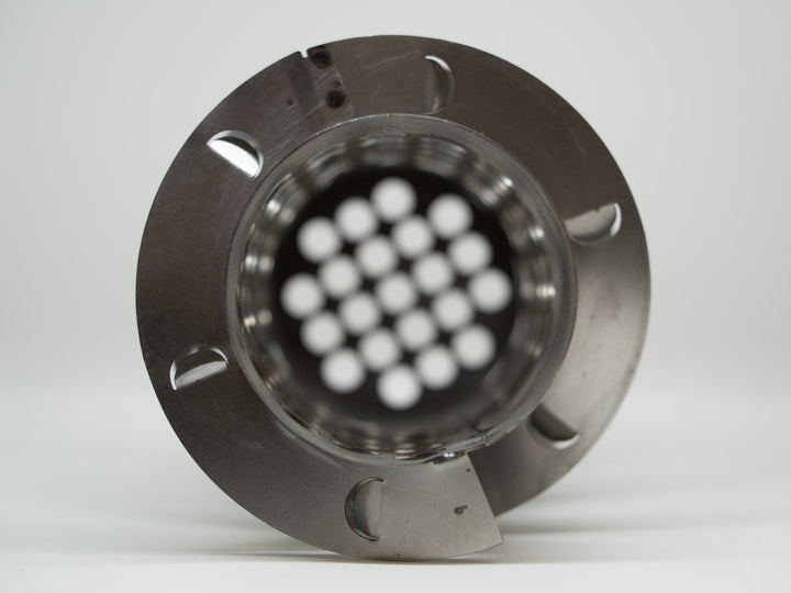 Metallic component with white spherical objects inside on a gray background
