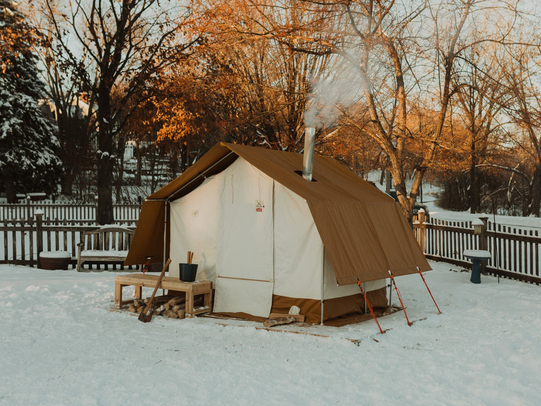 Sauna tent in a snowy outdoor setting with trees and a wooden fence.
