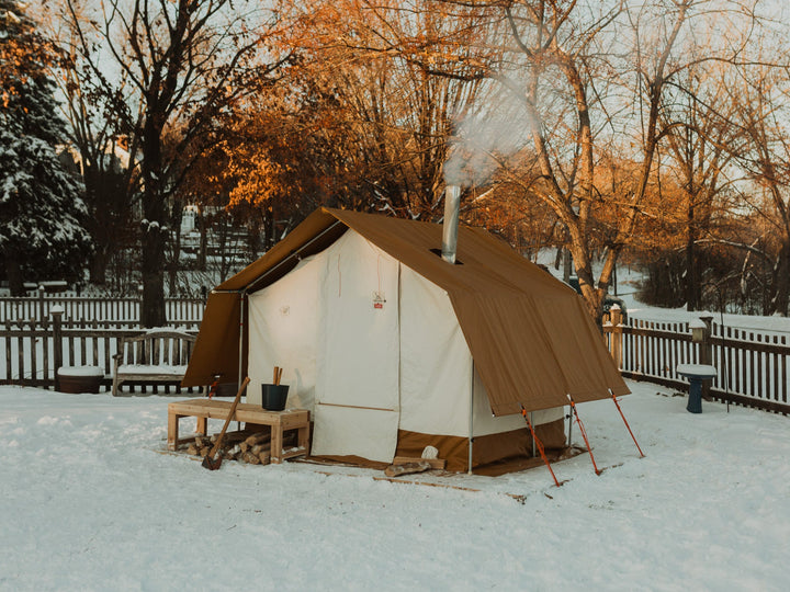 Sauna tent in a snowy outdoor setting with trees and a wooden fence.
