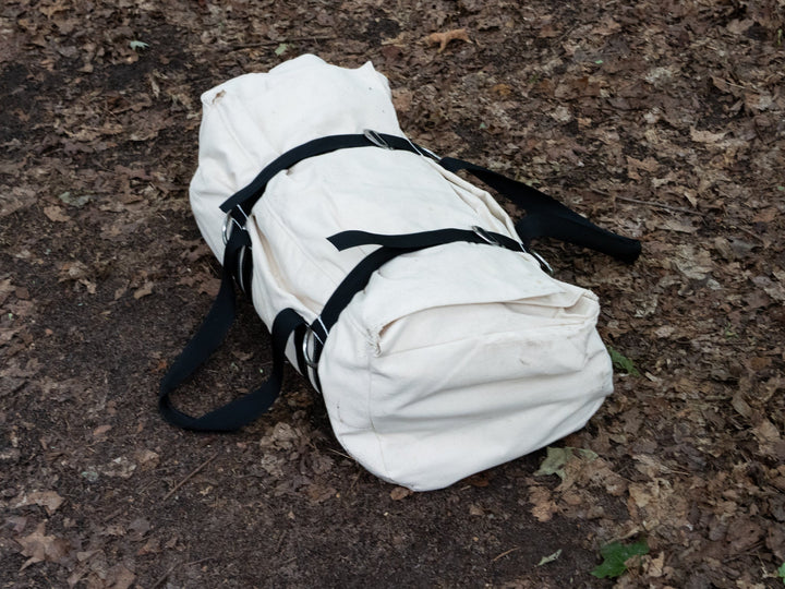 White duffel bag with black straps on a brown ground surface