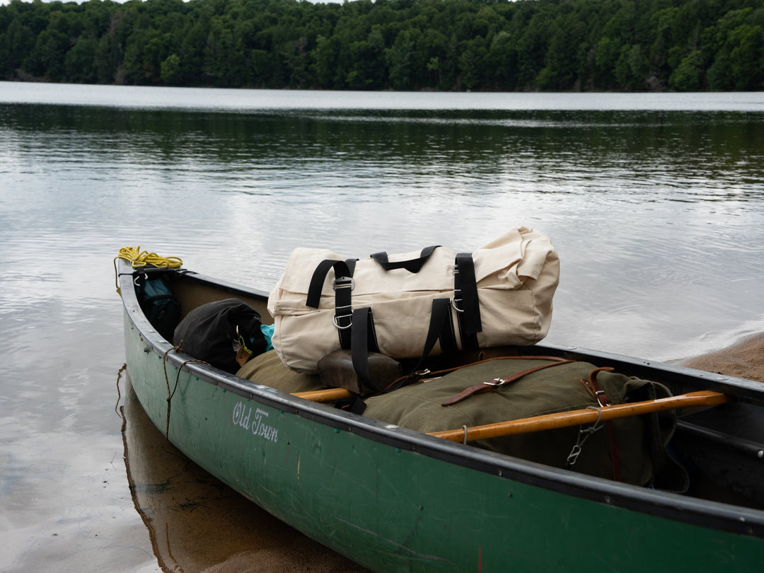 Canoe on a lake with camping gear, including a duffel bag and backpack.