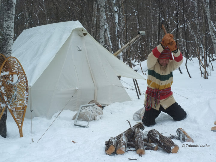 Snowtrekker 8x10 Shortwall with Tent Fly setup in snow man chopping wood with axe in front of tent trees in background