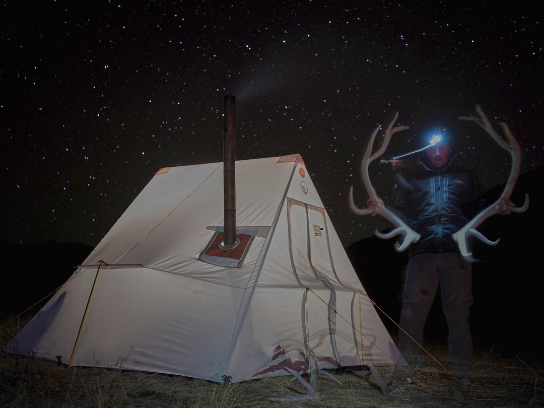 Person with large antlers standing next to a tent under a starry sky