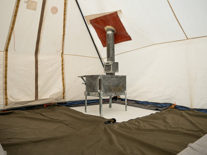 Metal stove inside a tent with a white interior and brown floor.
