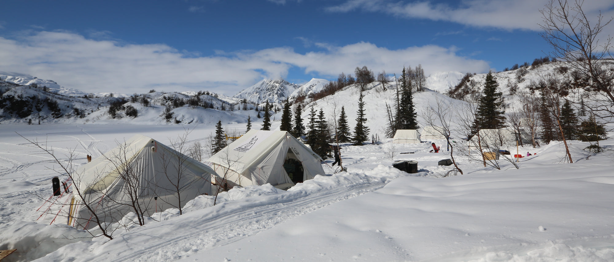 Winter scene of several Snowtrekker Tents set up in the snow with mountains in the background